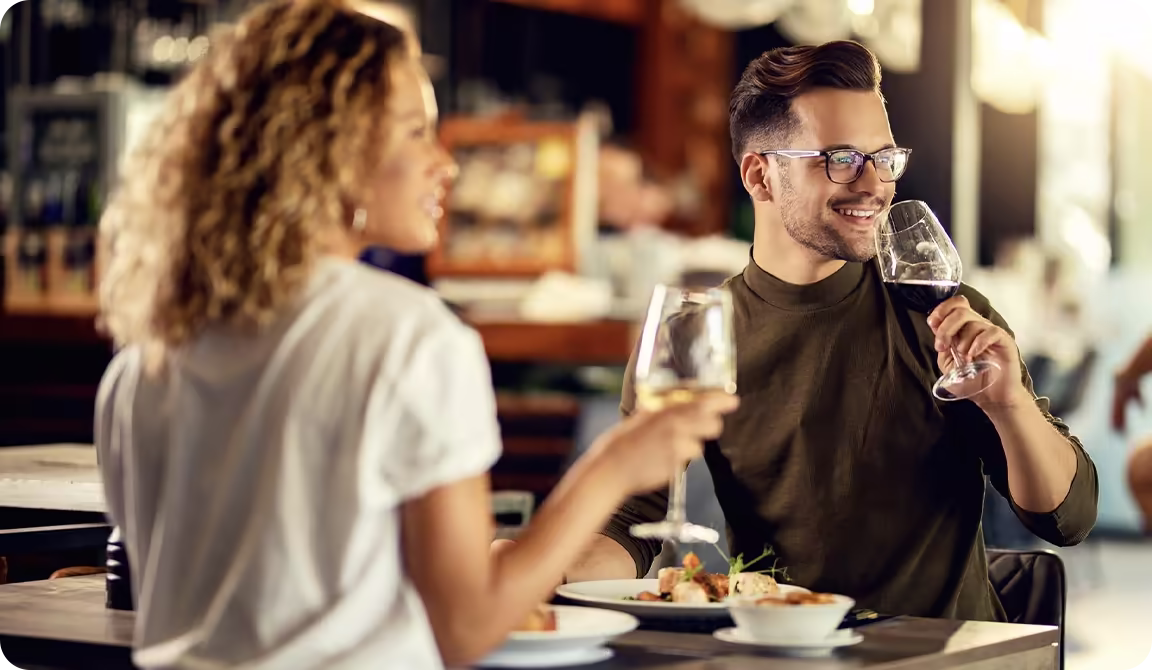 Usměvavý pár si vychutnává jídlo v restauraci se sklenkami vína.